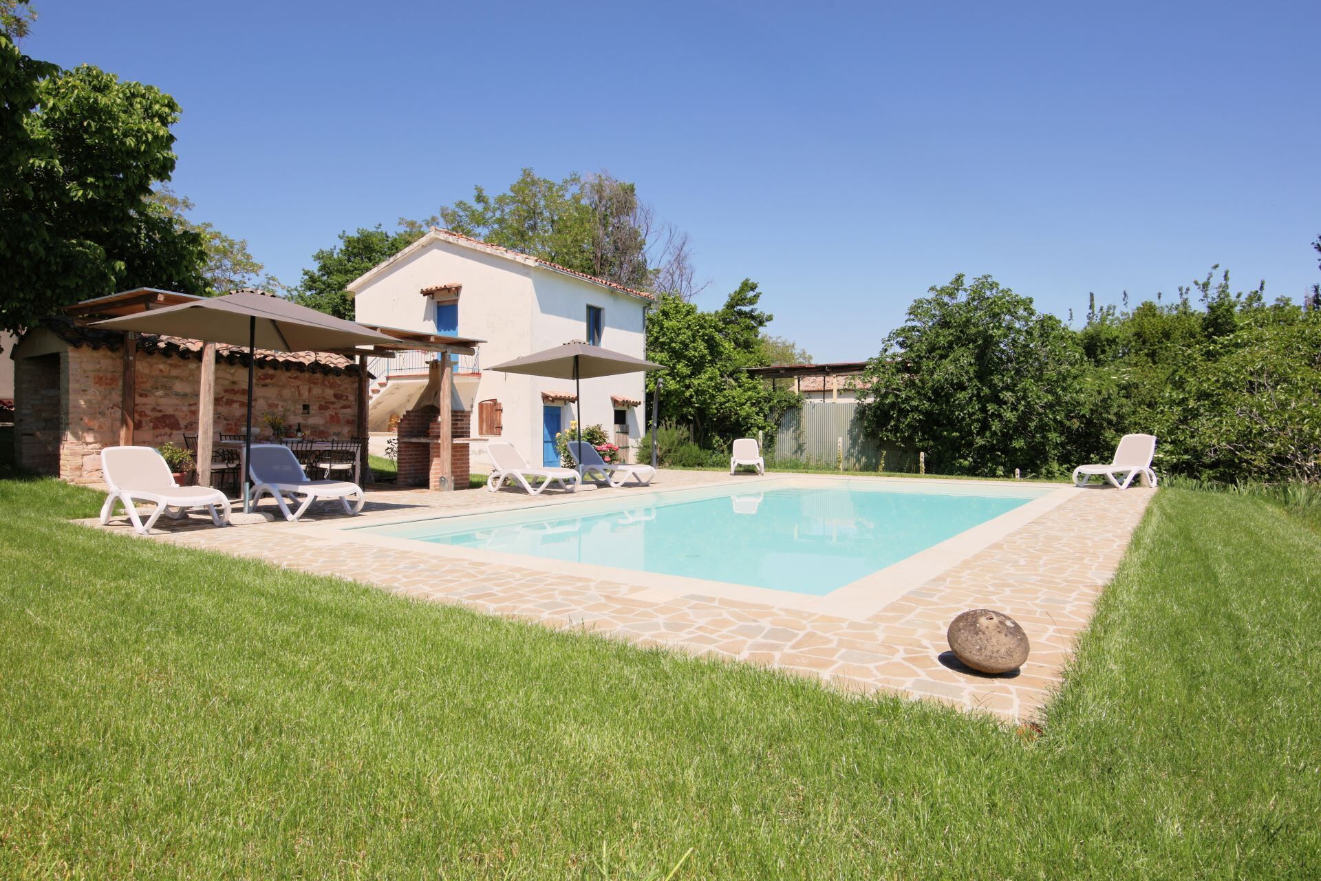 A pool area with lounge chairs, a barbecue setup, and a stone patio.