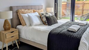 A bedroom with a large bed, a bedside table, a lamp, and a view of the outdoors through a sliding glass door.