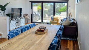A modern dining area with a wooden table and blue patterned benches, a kitchen with a TV, and a sliding glass door leading to an outdoor patio.