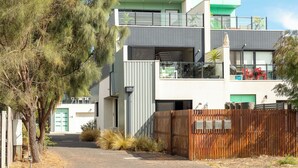 A modern two-story house with a covered outdoor area, a visible staircase, and a fenced front yard.
