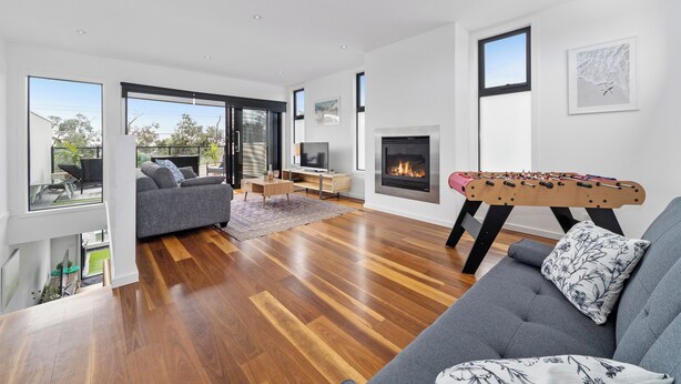A modern living room with a grey sofa, wooden flooring, a foosball table, and a fireplace.
