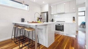 A modern kitchen with white cabinets, a central island with stools, a built-in oven, and a large window above the sink.