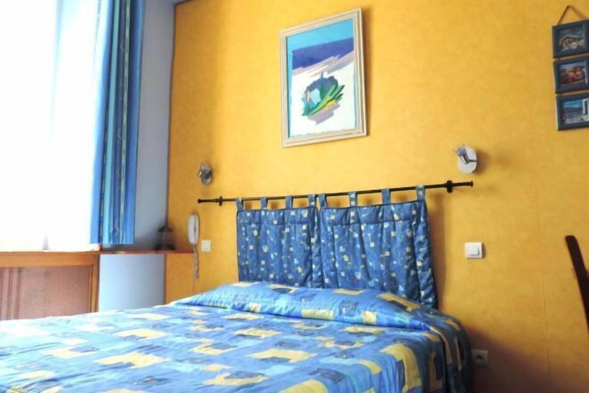 Quarto com cama, janela com cortinas, relógio de parede e quadro.