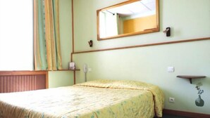 A hotel room with a bed, a mirror, a bedside table, and a wall-mounted shelf. - Hotel Provence by Adonis (Digne-les-Bains)