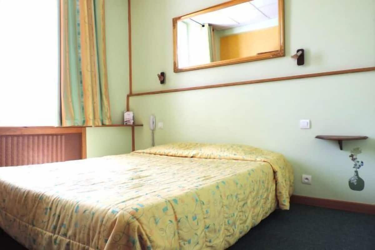 Quarto de hotel com uma cama, espelho, mesa de cabeceira e prateleira na parede.