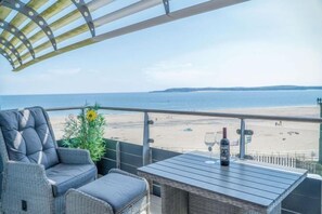 Un balcone con mobili in vimini, un tavolo con bottiglia e bicchiere, e vista sulla spiaggia e sul mare.