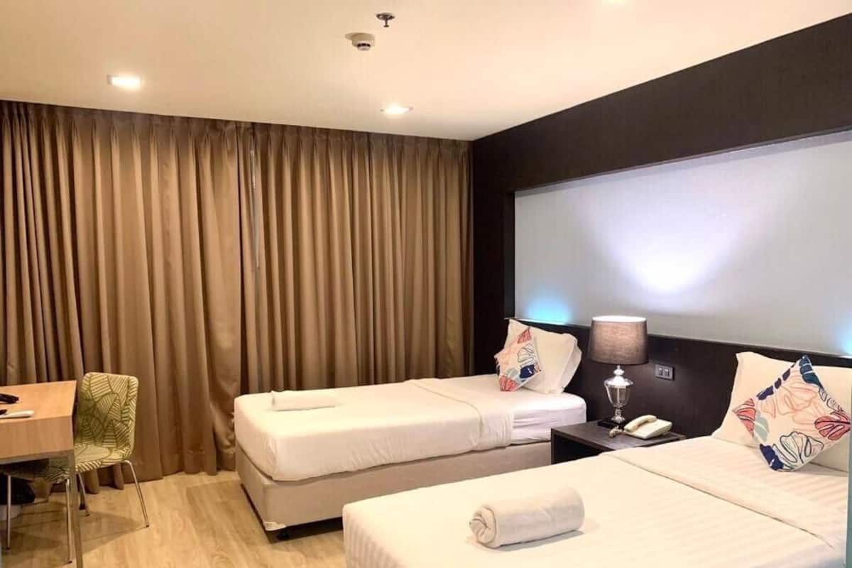 A hotel room with two beds, a desk, a chair, and a large window.