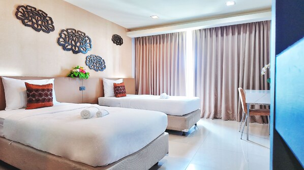 A hotel room with two beds, a desk, and a large window with curtains.
