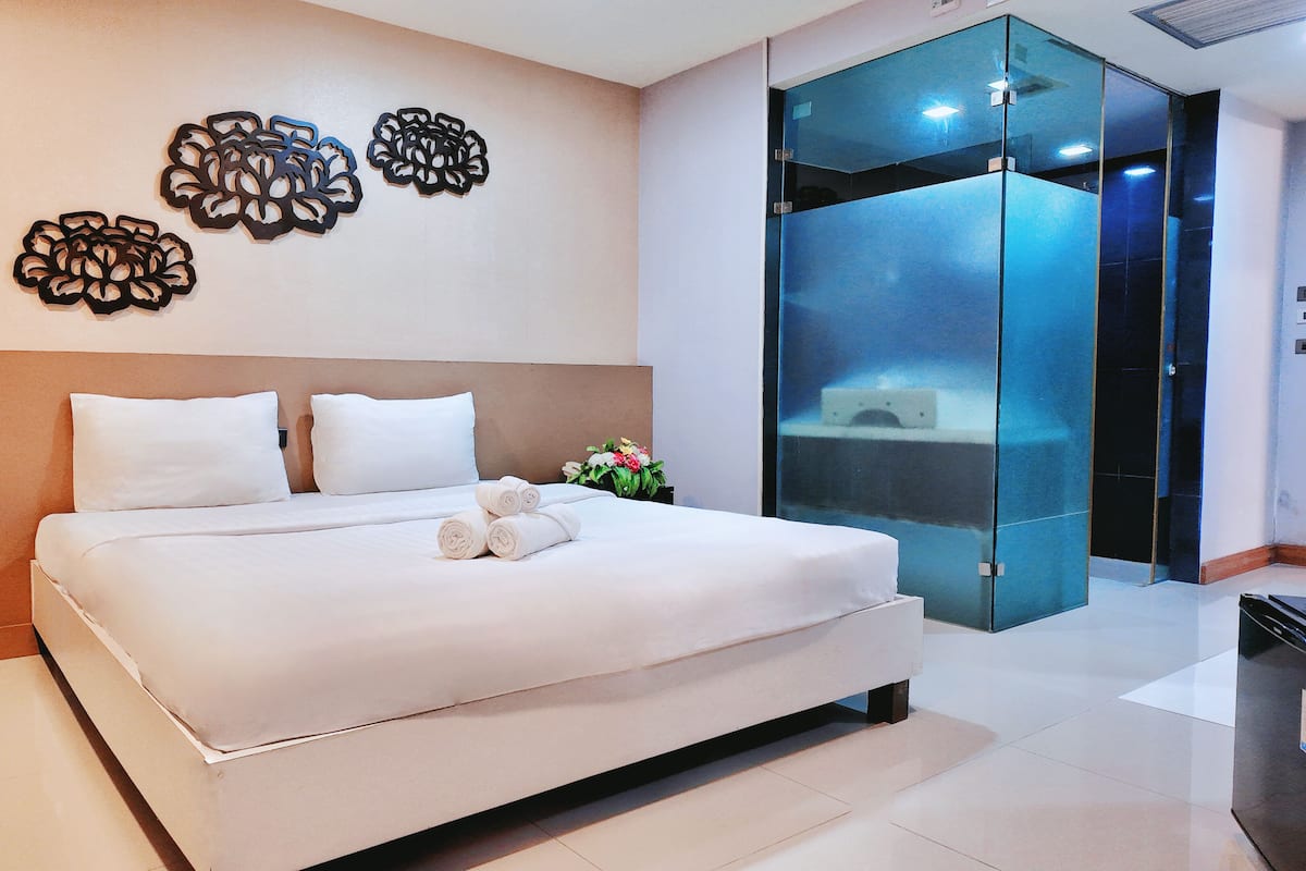 A modern hotel room with a large bed, a glass elevator, and decorative wall art.