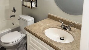 A bathroom with a toilet, sink, and shower. There are shelves with toiletries and a mirror above the sink. - Spacious 2-bedroom townhouse-style apartment located in the center of Dothan. (Dothan)