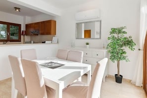 A modern kitchen with wooden cabinets, a white dining table with chairs, a potted plant, and a large mirror on the wall. - Villa HG33 Kornos (Kouklia)