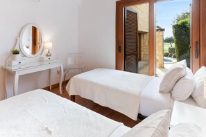 A bedroom with two beds, a white dresser with a mirror, a lamp, and a view of the outside. - Villa HG33 Kornos (Kouklia)