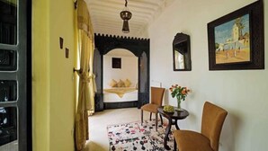 A room with a bed, a chair, a small table with flowers, and a painting on the wall. - Riad Azzar (Marrakech)