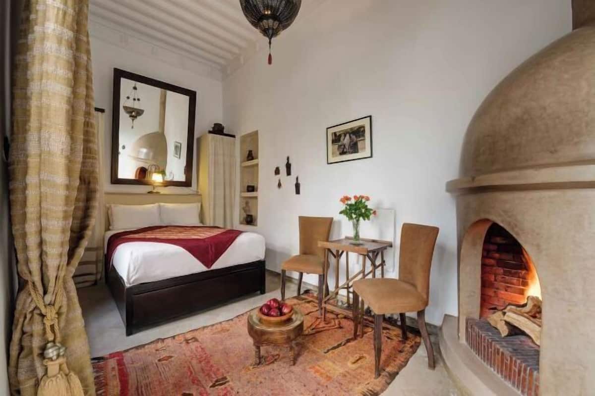 Ein Schlafzimmer mit einem Bett, einem Kamin, einem Tisch mit Stühlen und einem Spiegel.