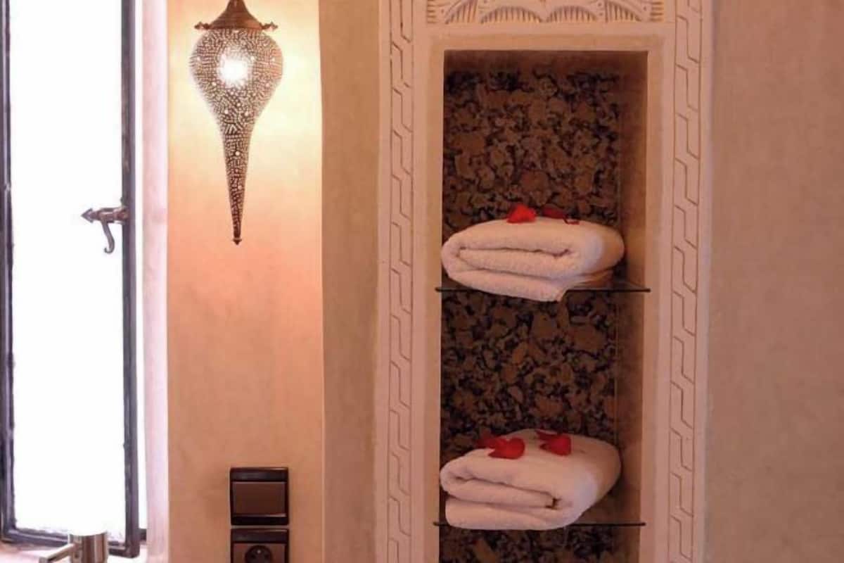 Ein Badezimmer mit einem an der Wand montierten Handtuchhalter, gefalteten Handtüchern, einer dekorativen Wandleuchte und einer strukturierten Wand.