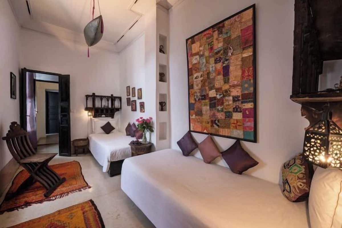 Ein Schlafzimmer mit zwei Betten, einer Hängelampe, einer Steppdecke und einem Holzstuhl.