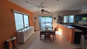 A modern kitchen with a dining area, large windows, and a ceiling fan.