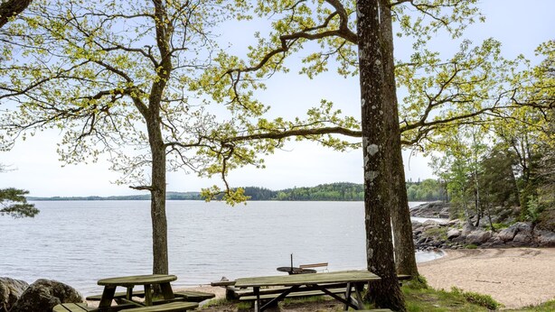 A lakeside picnic area with wooden benches and picnic tables, surrounded by trees and a view of the lake. - Klägghult by Interhome (Kalv)