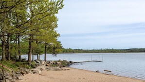 A sandy beach with a wooden bench, trees, and a calm lake. - Klägghult by Interhome (Kalv)