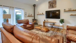 A cozy living room with leather sofas, a flat-screen TV, a fireplace, and wooden shelves. - Yosemite Quail Ridge Comforts with WiFi and Hot tub (Mariposa)