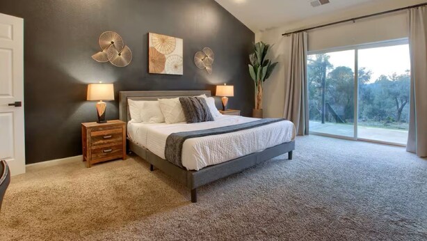 A bedroom with a large bed, two bedside tables with lamps, a dark accent wall, and a large window with curtains. - Yosemite Quail Ridge Comforts with WiFi and Hot tub (Mariposa)