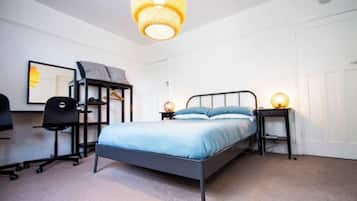 A bedroom with a bed, a desk, a chair, a wardrobe, and a hanging light fixture.