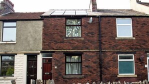 A two-story brick house with a stone wall in front, a red door, and a window with curtains. - Peaceful House in the Centre of City (Lancaster)