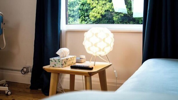 A hotel room with a bedside table, a lamp, a tissue box, and a remote control. - Peaceful House in the Centre of City (Lancaster)