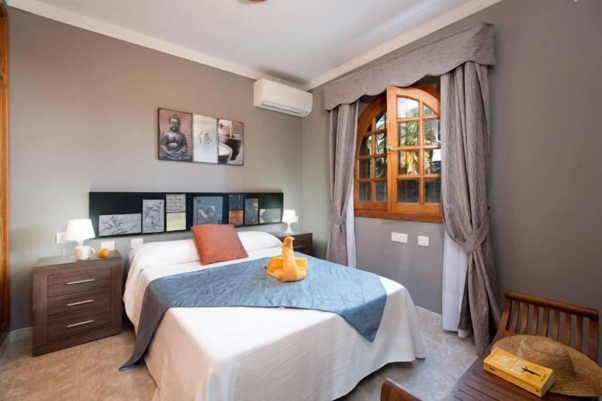 Un dormitorio con cama, mesitas de noche, una ventana con cortinas y decoración en la pared.
