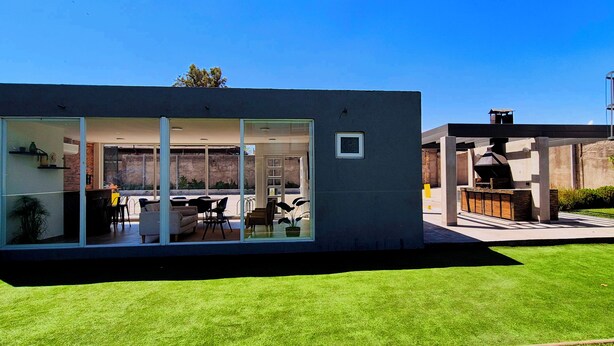 Una casa moderna con un patio cubierto de vidrio, una zona de barbacoa y un césped bien cuidado.
