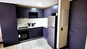 Una cocina compacta con armarios oscuros, horno empotrado y refrigerador.