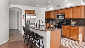 A modern kitchen with a central island, bar stools, wooden cabinets, stainless steel appliances, and a built-in microwave.