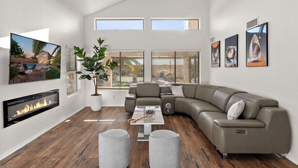A spacious living room with a large gray sectional sofa, a fireplace, and a large window overlooking a backyard.