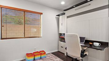 Une pièce comprenant un bureau, une chaise et des armoires de rangement. On y trouve une fenêtre avec des stores, un tapis et des boîtes de rangement colorées.