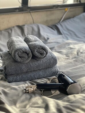 Una cama bien hecha con sábanas grises y una toalla enrollada encima.