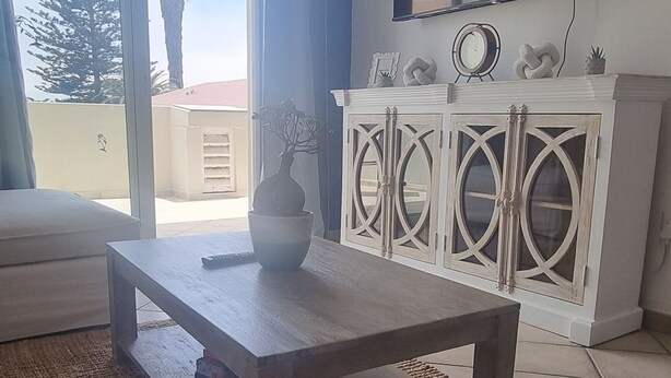 A living room with a sofa, a coffee table, a TV mounted on the wall, a cabinet with decorative items, and a view through a sliding door to the outside.