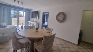 A dining area with a round table, wicker chairs, a television mounted on the wall, and a clock.