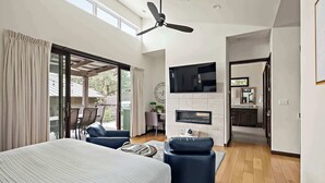 Un dormitorio con una cama, ventilador de techo, televisor y puerta corrediza de vidrio al exterior.