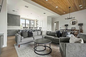 A spacious living area with a grey sectional sofa, a round coffee table, and a kitchen in the background.