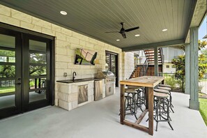 An outdoor kitchen with a stone wall, a grill, a sink, and bar stools.