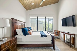 A bedroom with a bed, a desk, a TV, and a window.