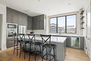 A modern kitchen with grey cabinets, a large window, and a central island with bar stools.