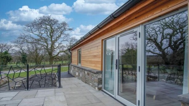 Un bâtiment moderne avec des fondations en pierre, un revêtement en bois et de grandes portes coulissantes en verre.