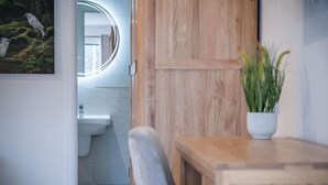 Une salle de bain avec un meuble en bois, un lavabo blanc et un miroir doté d’un éclairage circulaire.