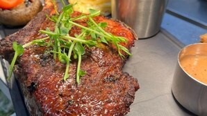 Un steak accompagné de légumes verts, une portion de frites et un petit bol de sauce.