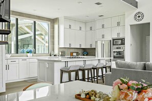 A modern kitchen with white cabinetry, a central island, and a dining area with a grey sofa.