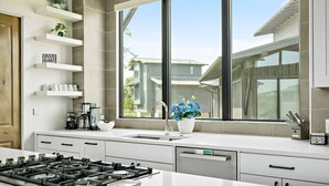 A modern kitchen with a gas stove, a sink, and a window with a view of neighboring houses. - Lake Travis Getaway / Pickleball / Grill / Firepit (Lake Travis)