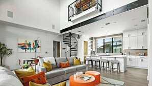 A modern living room with a grey sofa, orange ottoman, and a staircase leading to an upper level. - Lake Travis Getaway / Pickleball / Grill / Firepit (Lake Travis)