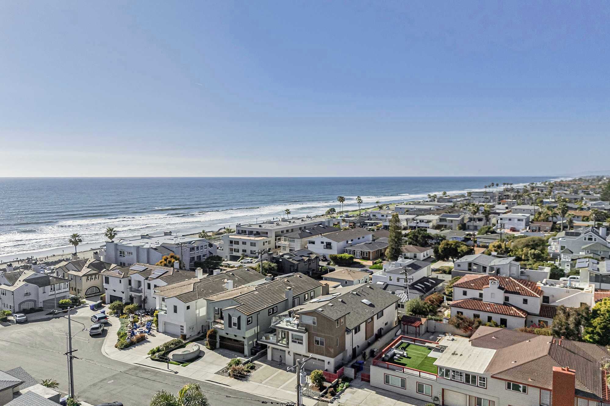 A coastal residential area with houses, a beach, and a clear sky.