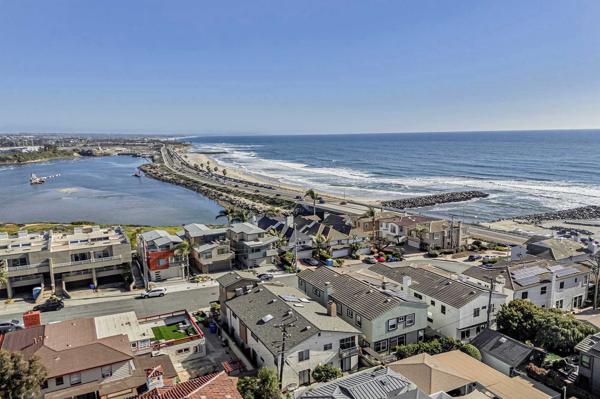 A coastal residential area with houses, a beach, and a rocky breakwater.